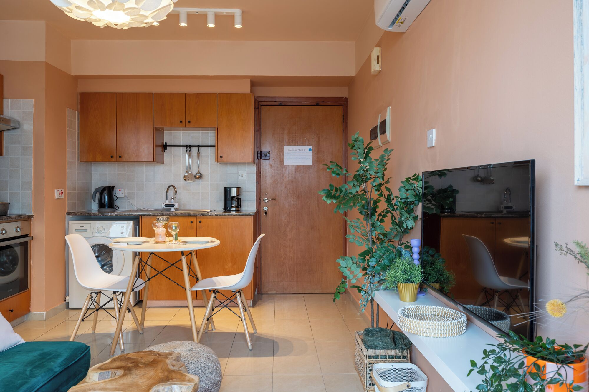 A compact kitchen with wooden cabinets, a dining area with a round table and chairs, a sofa, and a TV.
