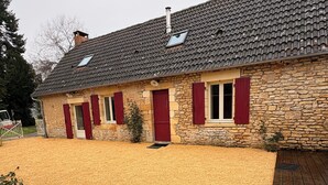 Un bâtiment en pierre avec un toit en tuiles, des volets rouges et une allée gravillonnée.