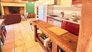 Une cuisine rustique avec des poutres apparentes, un sol carrelé et des équipements de base, notamment une cuisinière, un évier et un réfrigérateur.