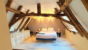 Une chambre avec un plafond en pente, des poutres en bois, un lit, des tables de chevet et une petite table.
