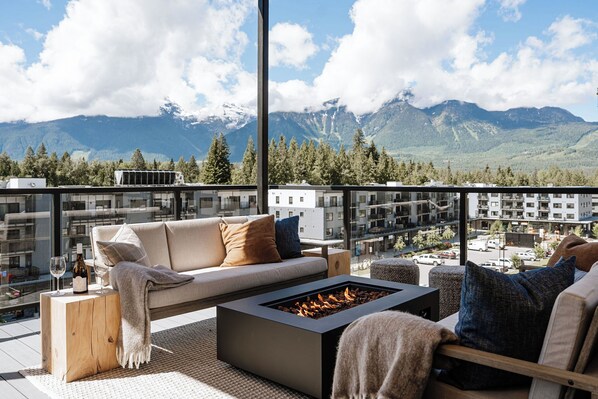 Un balcon moderne avec un canapé, un foyer extérieur et une vue sur les montagnes.