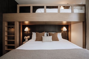Une chambre avec un lit superposé, une tête de lit en bois, des lampes de chevet et une petite table sur laquelle est posé un vase.