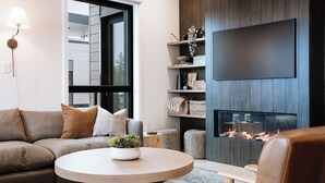 Ein modernes Wohnzimmer mit einer Couch, einem runden Couchtisch, einem Kamin und einem an der Wand montierten Fernseher.