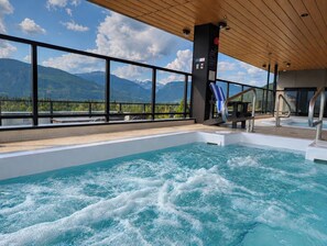 Un jacuzzi con vistas a las montañas, techo de madera y barandilla de vidrio.