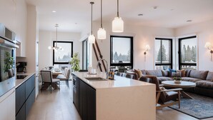Eine moderne Küche mit einer zentralen Kochinsel, einem Essbereich mit Tisch und Stühlen sowie einem Wohnbereich mit Sofa und Couchtisch.