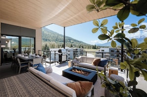 Un espace de vie extérieur moderne, doté d’un foyer, de sièges et offrant une vue sur les montagnes.