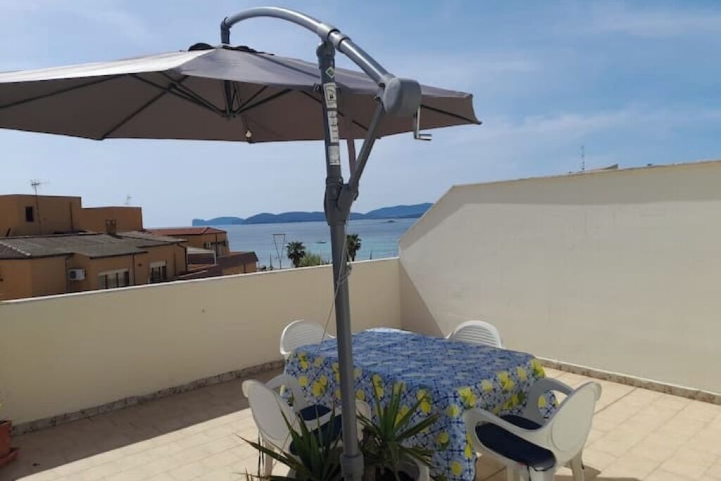 A balcony with a table and chairs, an umbrella, and a view of the sea.
