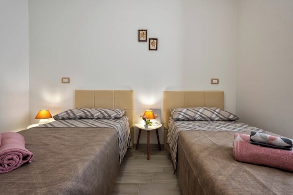 A hotel room with two beds, each with a headboard, a small table with a lamp, and a wall-mounted light fixture.