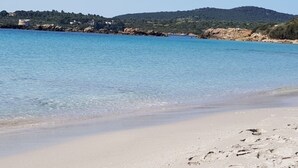 Een strand met helderblauw water, een zandstrand en een glooiend landschap op de achtergrond.