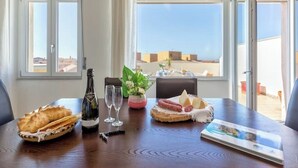 Een eettafel met champagne, glazen, een mand met brood, een bord met kaas en vleeswaren, en een tijdschrift.