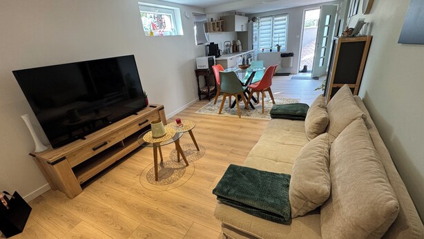 A living room with a TV, sofa, coffee table, and a kitchen in the background. - New, modern apartment • Comfort - Parking (Sundhoffen)