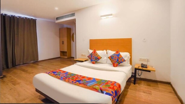 A hotel room with a large bed, a wooden headboard, a bedside table with a lamp, and a curtain on the window. - Ramayan Inn Hotel (Lucknow)
