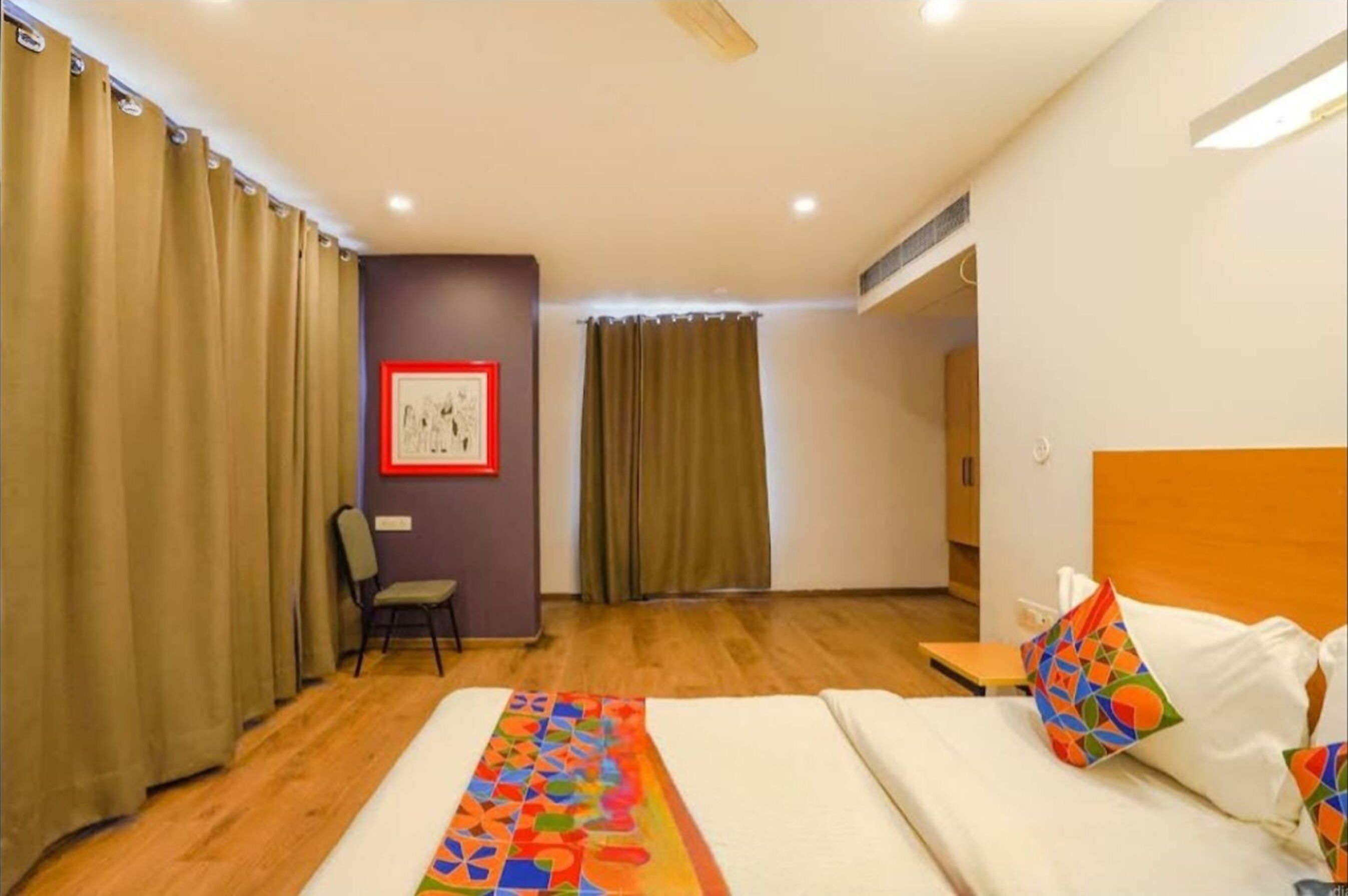 Een hotelkamer met een bed, een stoel, een inlijsting foto aan de muur en een raam met gordijnen.