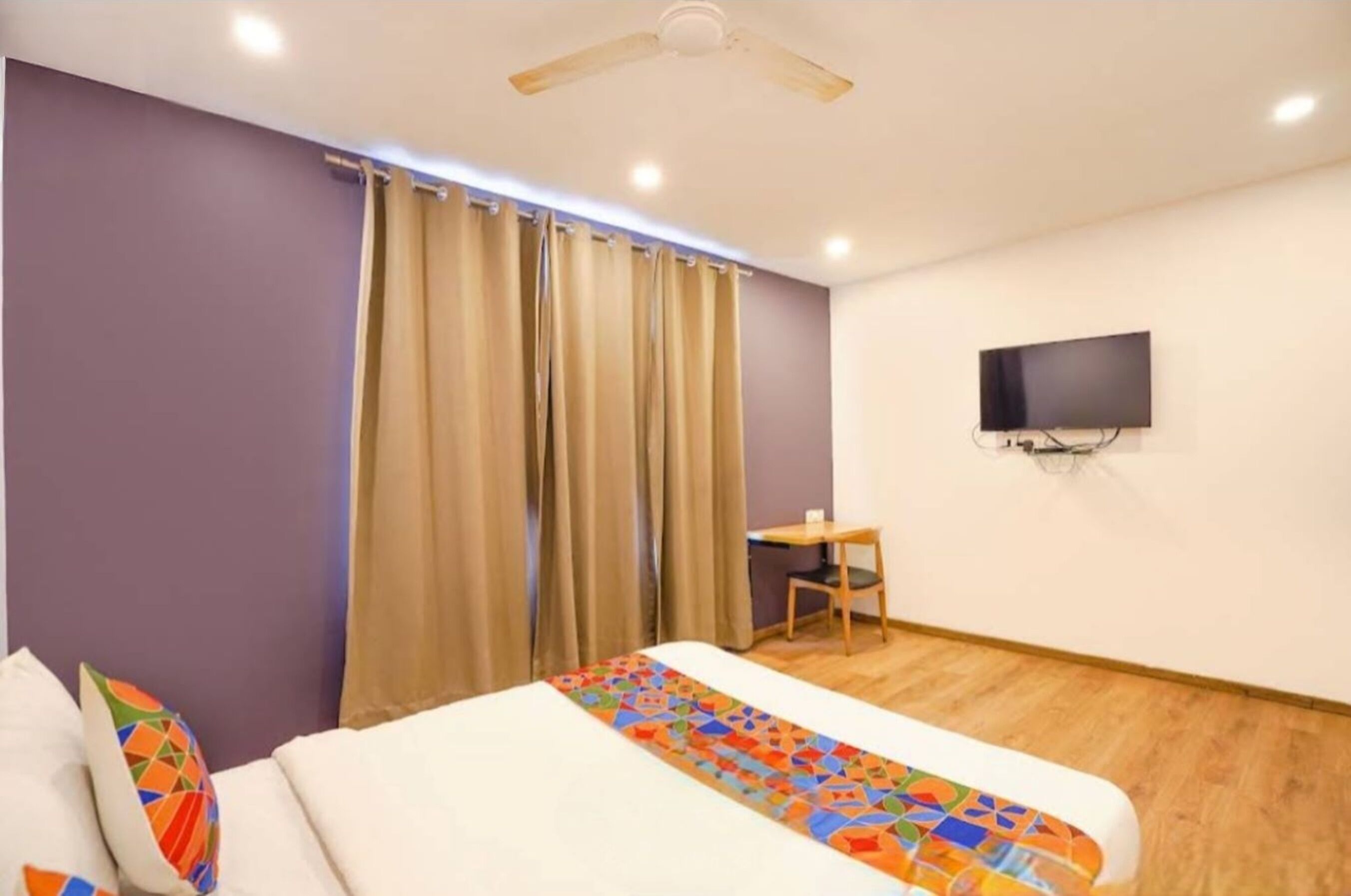 A hotel room with a bed, a desk, a television, and a ceiling fan.