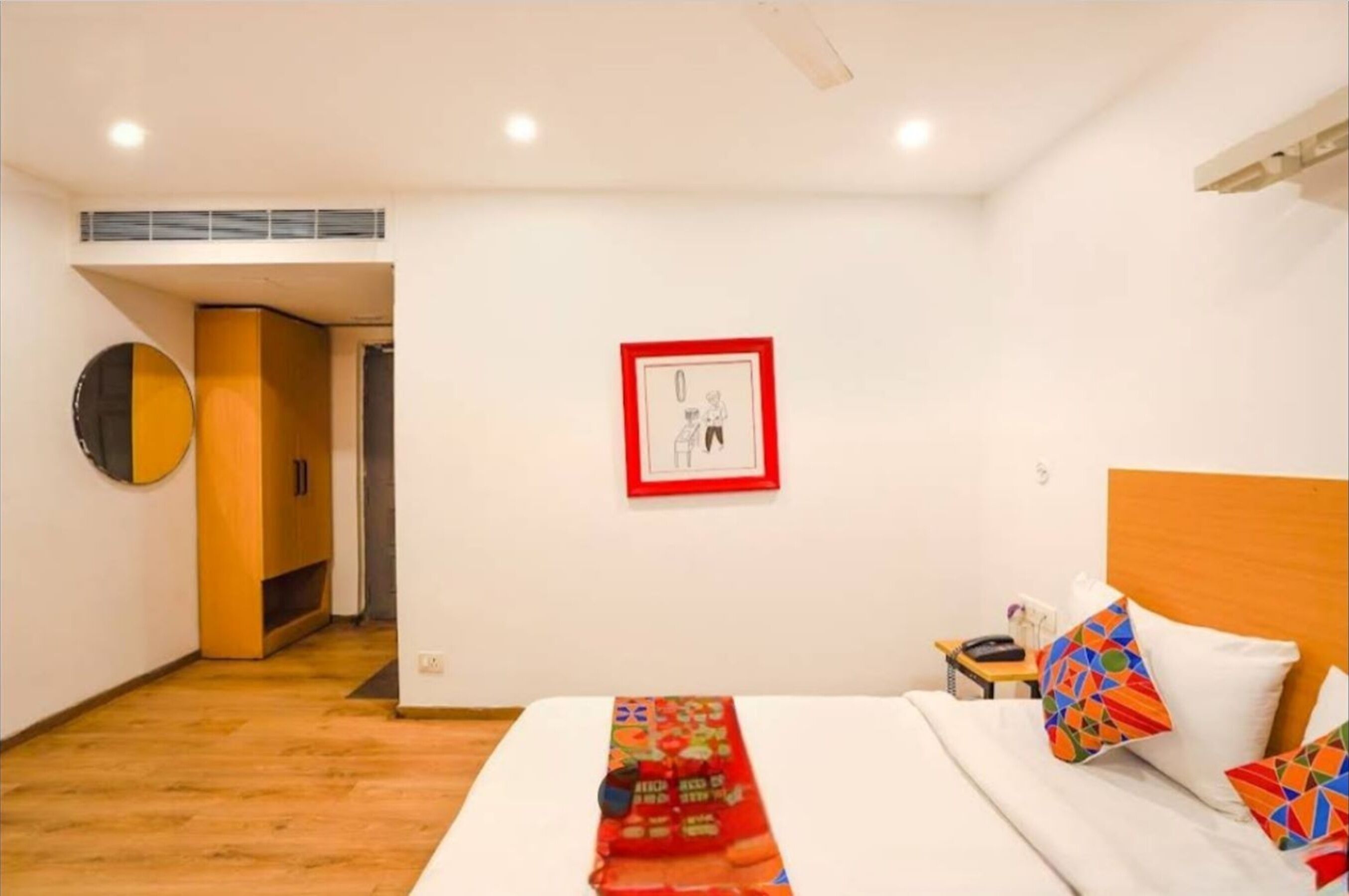 A hotel room with a bed, a nightstand, a wall-mounted picture, and a wooden cabinet.