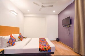 Een hotelkamer met een bed, een plafondventilator, een aan de muur bevestigde televisie en een gordijn voor het raam.
