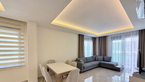 A modern living room with a dining area, a sectional sofa, and a TV. - SA Apartments! 2bd Duplex next to Cleopatra Beach (Alanya)