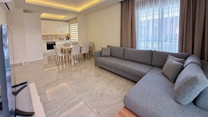 A modern living room with a grey sofa, a dining table with chairs, and a kitchen in the background. - SA Apartments! 2bd Duplex next to Cleopatra Beach (Alanya)