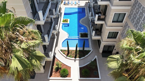 A multi-story hotel with a central swimming pool, balconies with sun loungers, and palm trees. - SA Apartments! 2bd Duplex next to Cleopatra Beach (Alanya)