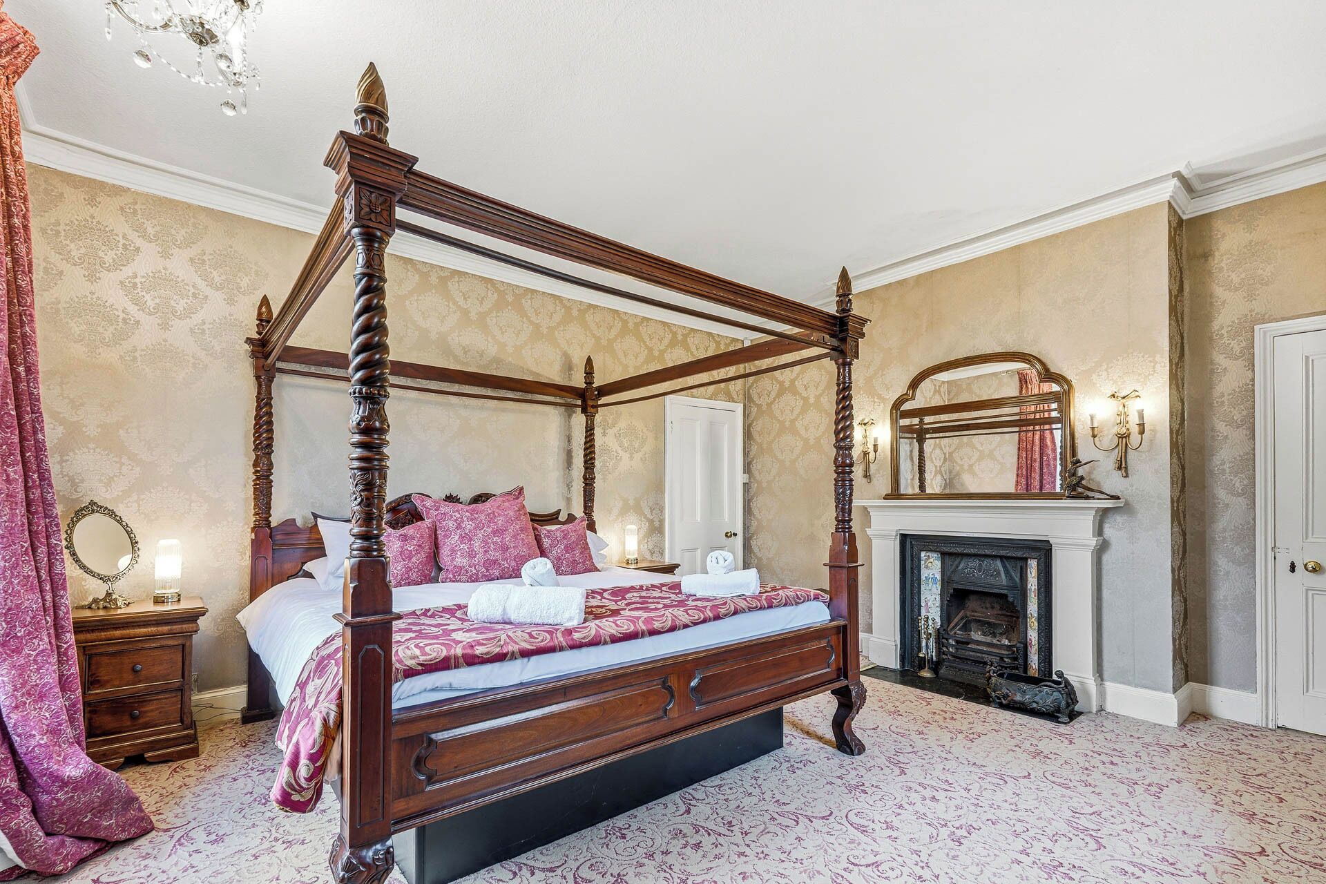 Ein Bett mit Baldachin, ein Spiegel darüber, ein Kamin und ein Nachttisch mit Lampe.