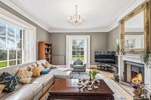 Een ruime woonkamer met een grote bank, een open haard, een televisie en een boekenkast.
