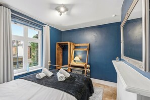 Een slaapkamer met een groot bed, een houten stoel, een spiegel en een raam met gordijnen.