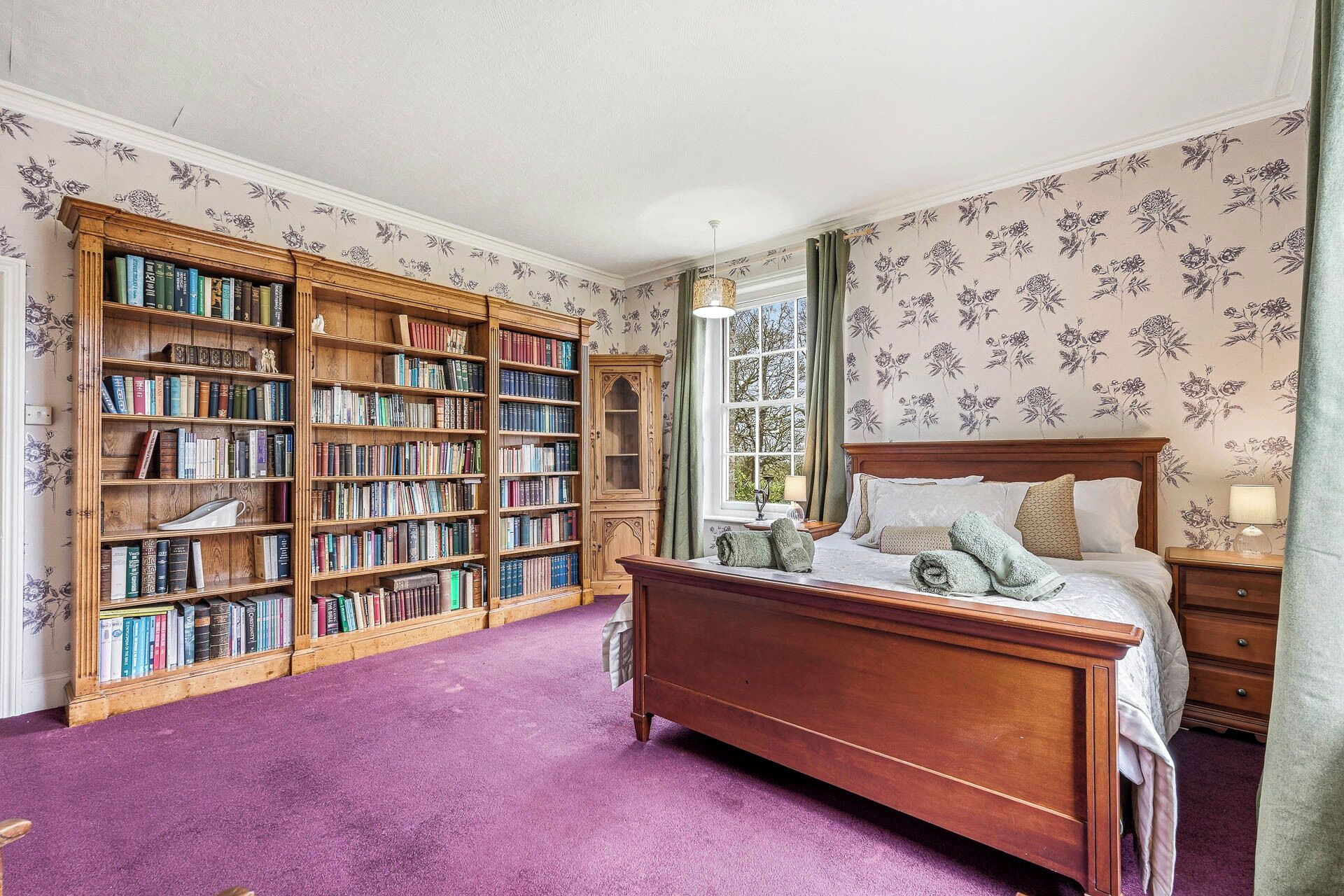 A bedroom with a large wooden bookshelf, a wooden bed, and floral wallpaper.