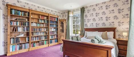 A bedroom with a large wooden bookshelf, a wooden bed, and floral wallpaper.