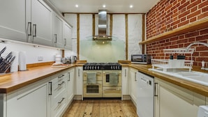 A modern kitchen with white cabinets, a brick wall, a stainless steel range hood, a microwave, and a sink with a dish rack.