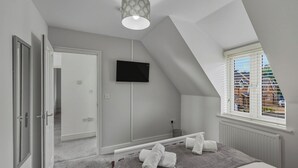 Ein Schlafzimmer mit schrägverdachter Decke, einem an der Wand montierten Fernseher, einem Fenster mit Jalousien und einem Bett mit Handtüchern.