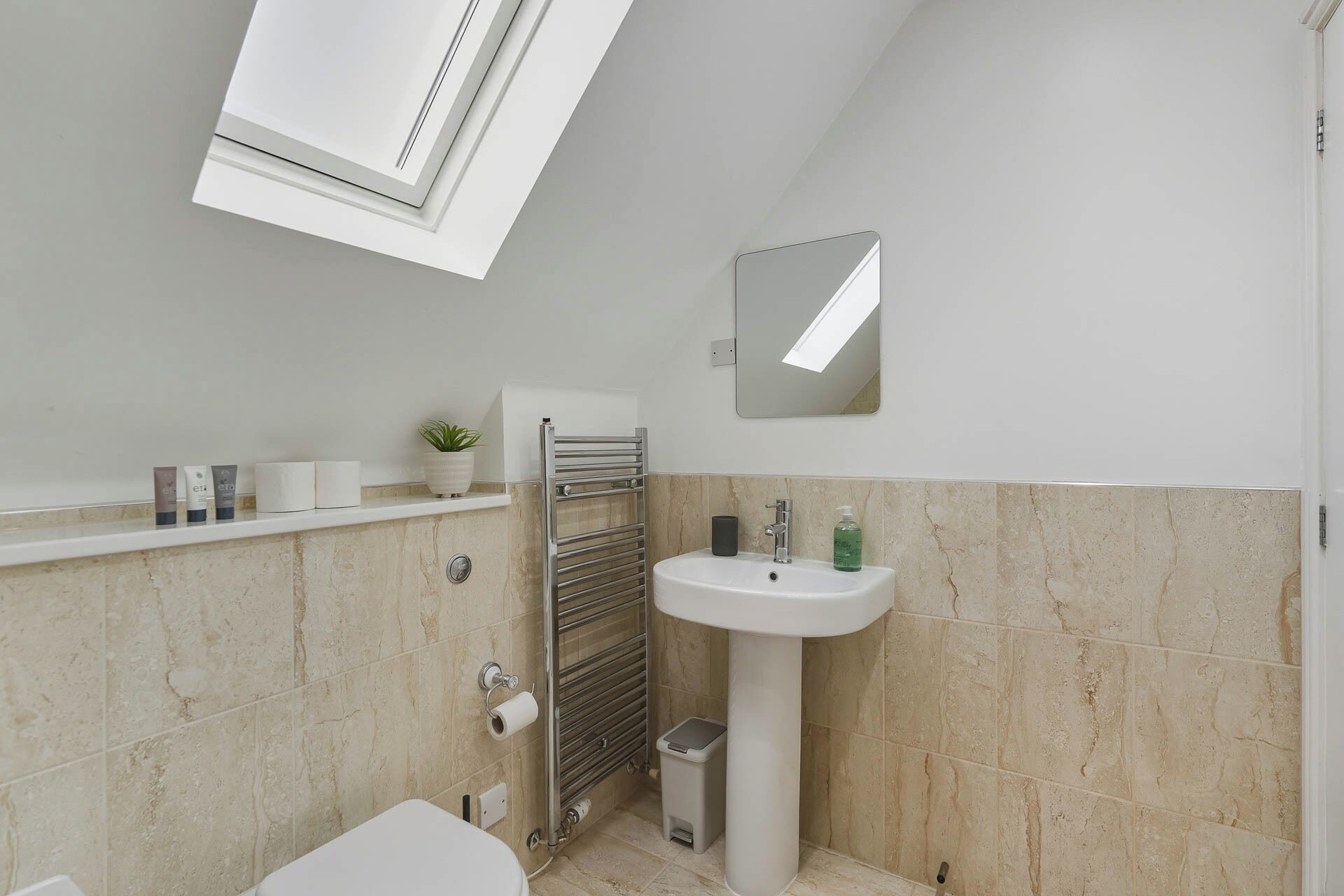 A modern bathroom with a toilet, sink, towel rack, and a small trash bin.