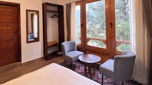 A hotel room with a bed, two armchairs, a small table, a wardrobe, and a window with a view of trees. - The Zen Punakha (Punakha)