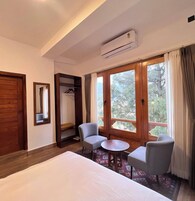 Habitación de hotel con cama, dos sillones, una mesita, un armario y ventana con vistas a árboles.