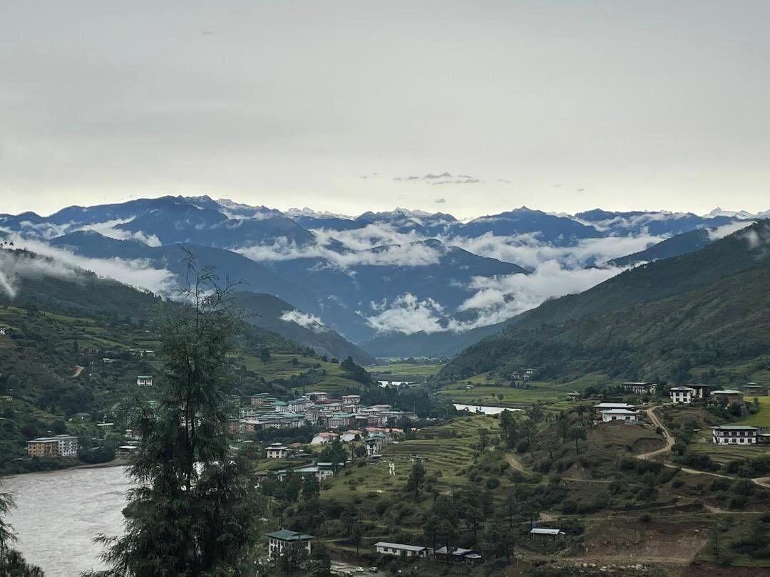 A valley with a river, houses, and mountains in the background.