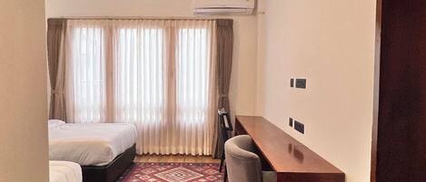 A hotel room with two beds, a desk, a chair, a patterned rug, and an air conditioning unit.