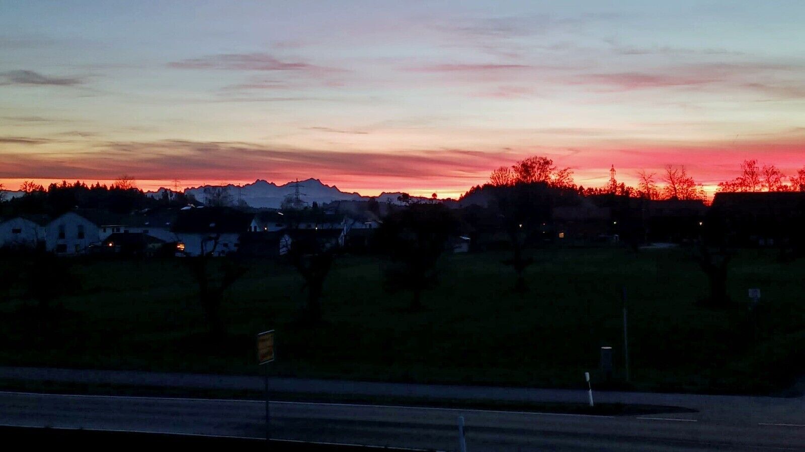 A sunset view with houses and trees in the foreground.