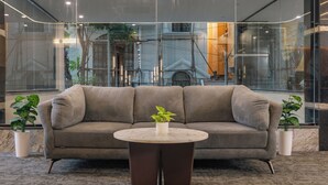 A modern living room with a grey sofa, a round coffee table, and two potted plants. - U By Z Hotels, Brookefield (Bengaluru)