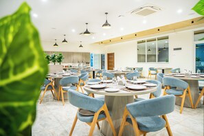 Un espace de restauration moderne avec des tables rondes, des chaises recouvertes de tissu bleu et des luminaires suspendus.