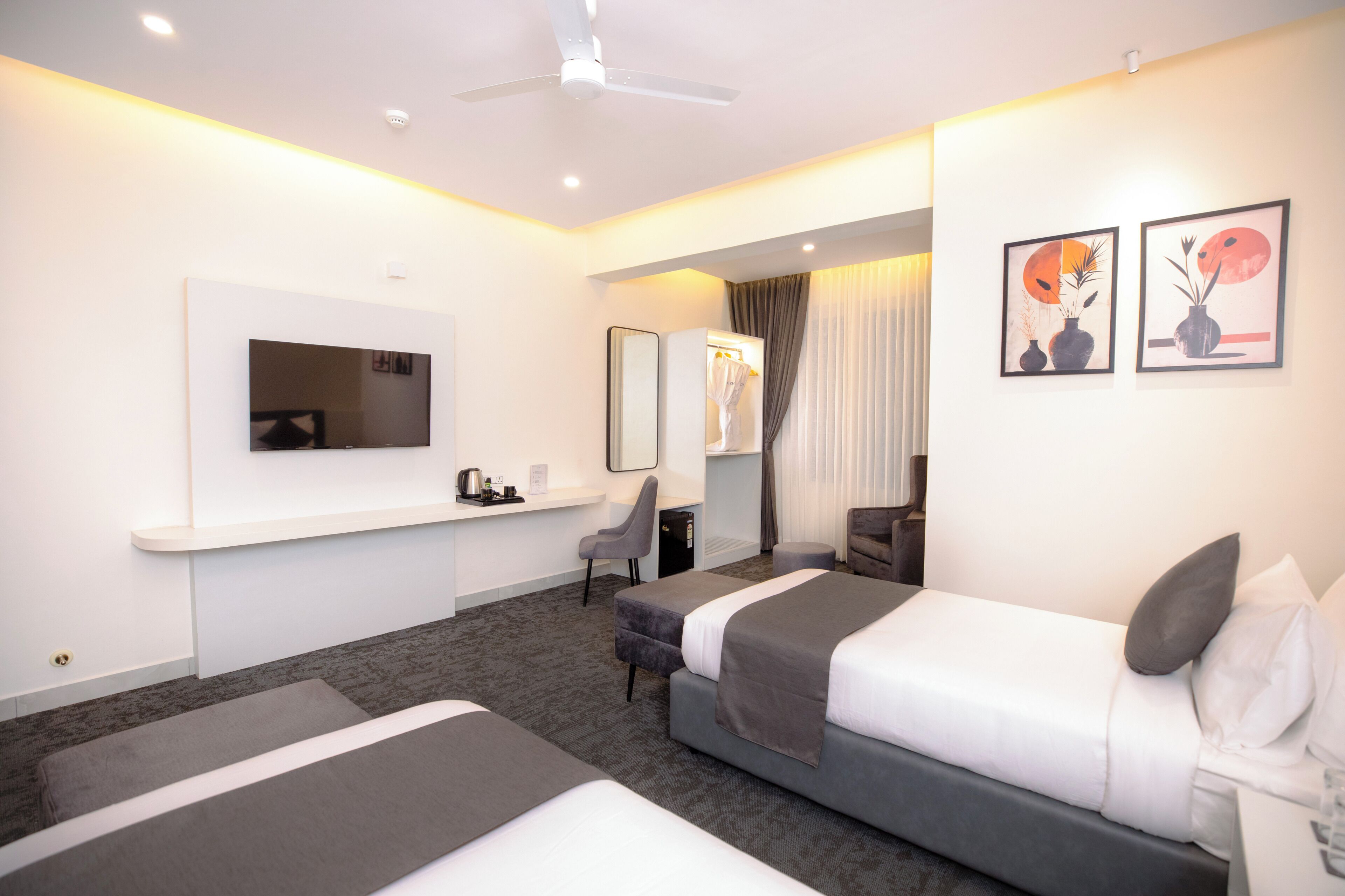A hotel room with two beds, a desk with a chair, a mirror, and artwork on the wall.