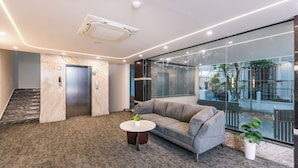 A modern lobby with a marble reception desk, a grey sofa, a small round table with a plant, and a glass wall offering a view of the outside. - U By Z Hotels, Brookefield (Bengaluru)