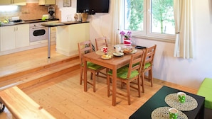 Une cuisine chaleureuse avec des meubles de rangement en bois, une table à manger avec des chaises et une fenêtre agrémentée de rideaux.