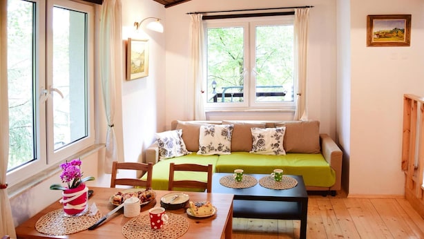 Une pièce chaleureuse avec un plancher en bois, un canapé vert, une table à manger en bois avec des chaises, et une fenêtre avec des rideaux.