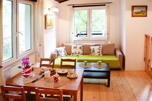 A cozy room with a wooden floor, a green sofa, a wooden dining table with chairs, and a window with curtains. - Lakeside Holiday Home With Private Garden (Szemud)