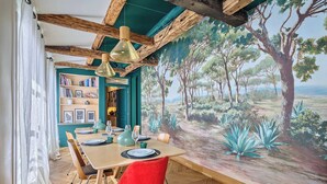 Uma sala de jantar com um mural de uma floresta e do mar, vigas de madeira e uma mesa posta para dois.