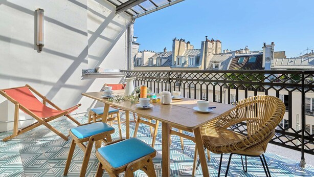 Terraço no telhado com mesa, cadeiras e vista para prédios da cidade.