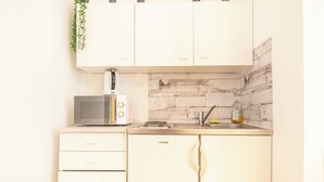 A kitchen with white cabinets, a microwave, a toaster, a sink, and a hanging plant. - Lovely 2BR Near Belvedere Palace (Vienna)