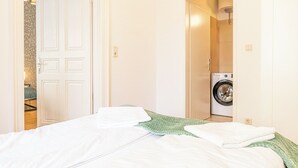 A bedroom with a bed, a washing machine, and a door leading to another room. - Lovely 2BR Near Belvedere Palace (Vienna)