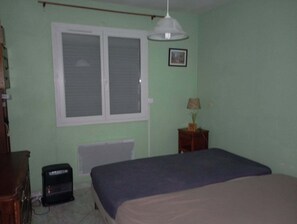A bedroom with a bed, a radiator, a window, a bedside table with a lamp, and a small speaker. - Detached house with fenced garden and rear terrace (Le Boulou)