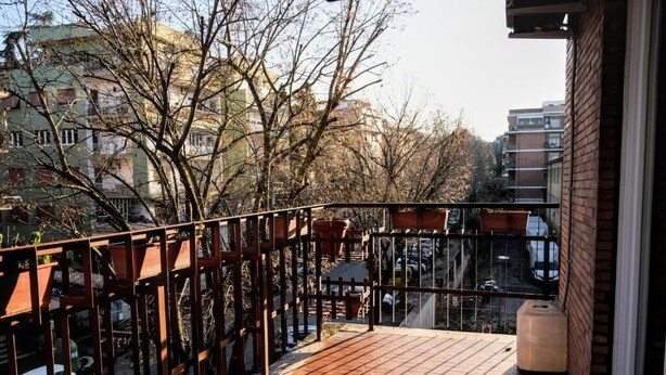 Un balcone con pavimento in legno, ringhiera metallica e vista su una strada con auto e palazzi.