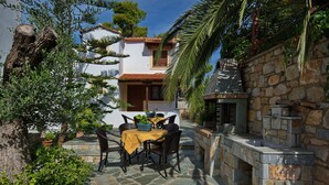 Eine mit Steinen gepflasterte Terrasse mit Tisch und Stühlen, umgeben von Grünpflanzen und einer Steinmauer.
